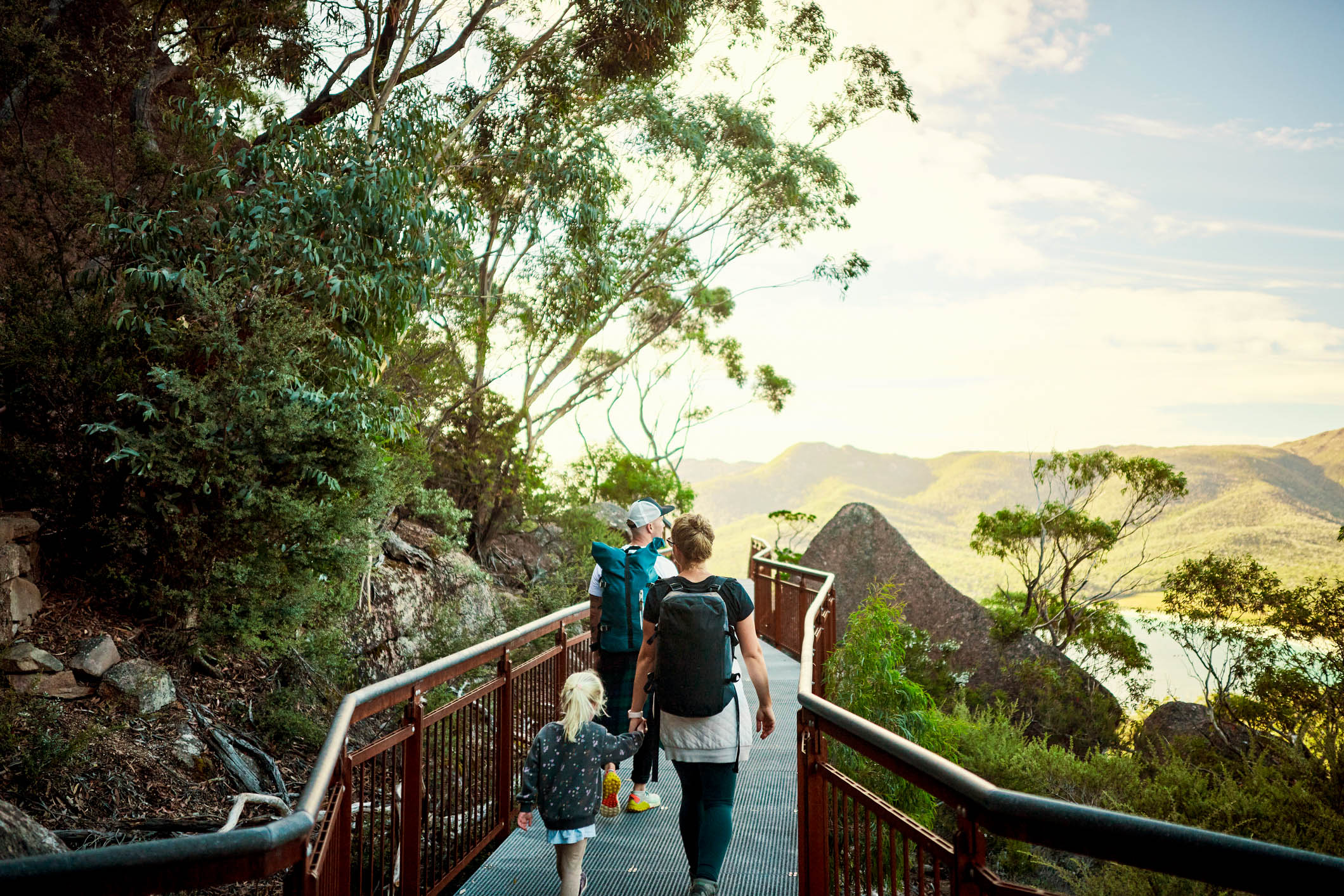 Two parents and a small child walk together on a railed pathway in the Australian bush